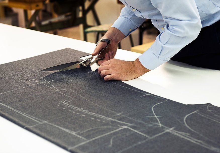 Tailor cutting dark fabric along chalk pattern lines with large shears