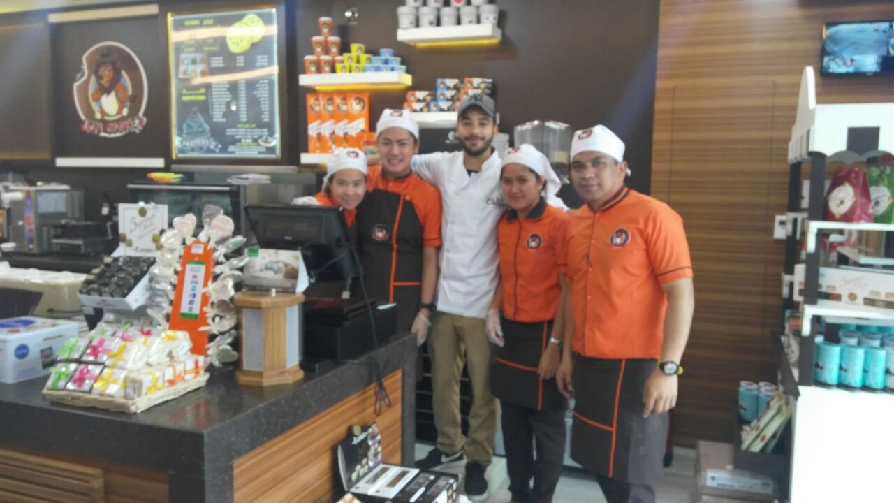 Shop staff in orange uniforms and white caps standing behind a store counter