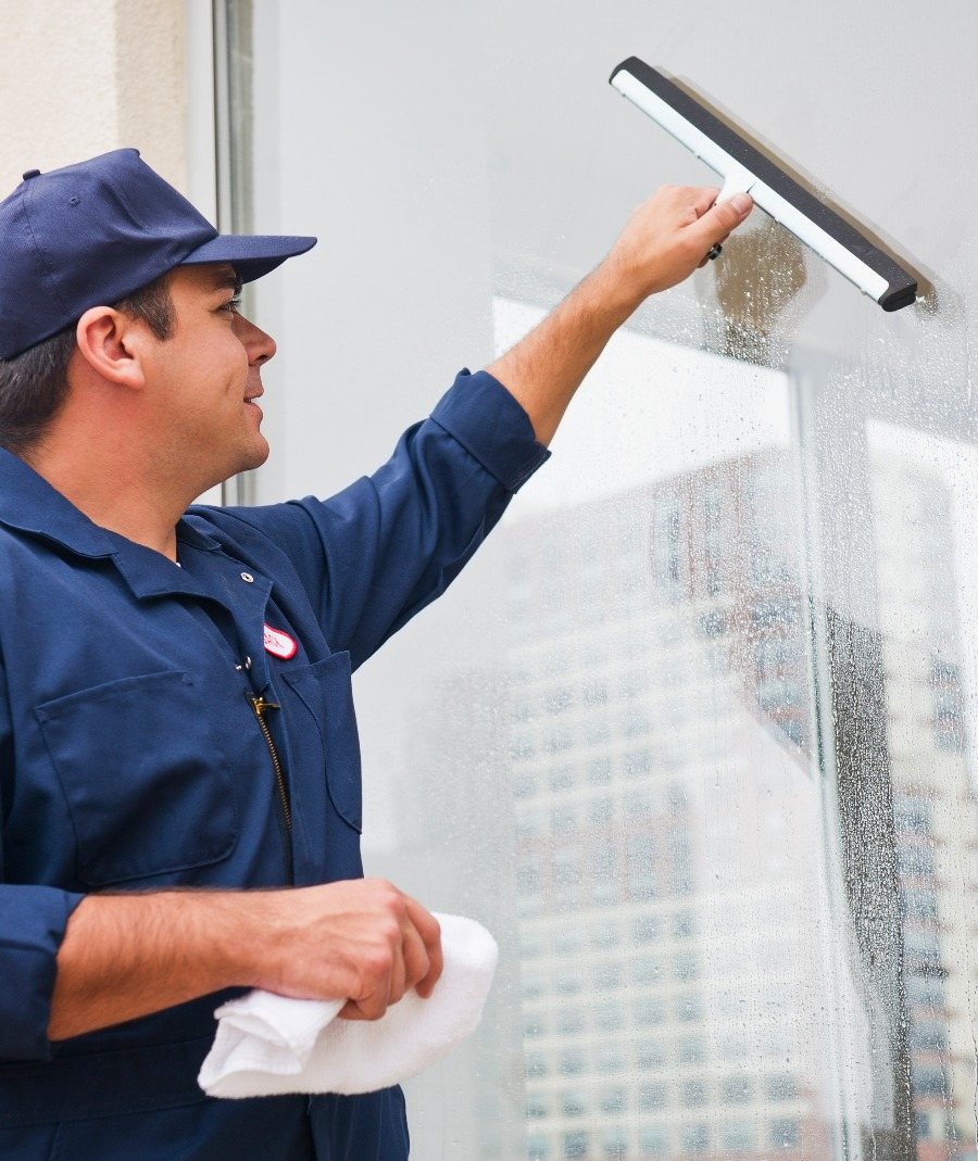 Window cleaner in a navy uniform and cap wiping a glass pane with a squeegee