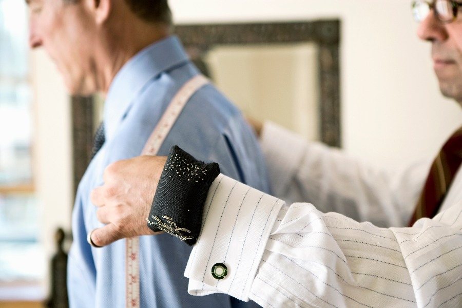 Tailor in a shirt and tie measuring a client's arm with a tape measure